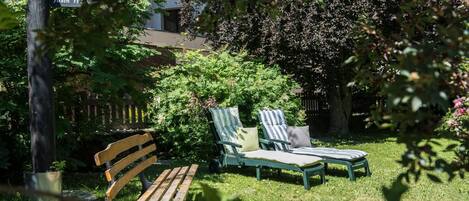 Un jardín con un banco de madera y dos sillones a rayas.