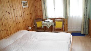 A wooden-paneled room with a bed, a small table with chairs, and a window with curtains.