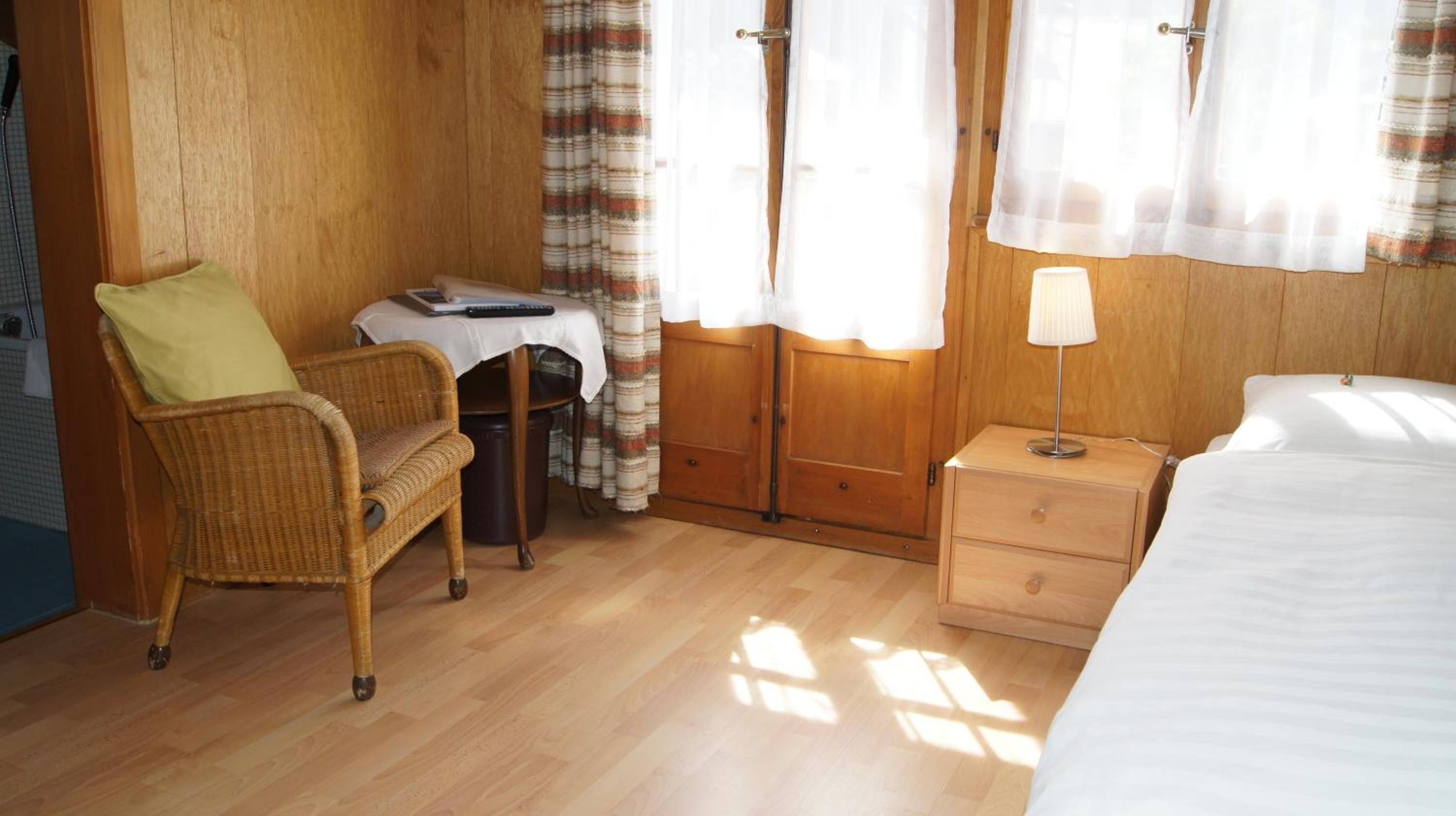 A room with a bed, a chair, a small table with a laptop, a lamp, and curtains.