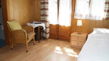 A room with a bed, a chair, a small table with a laptop, a lamp, and curtains.