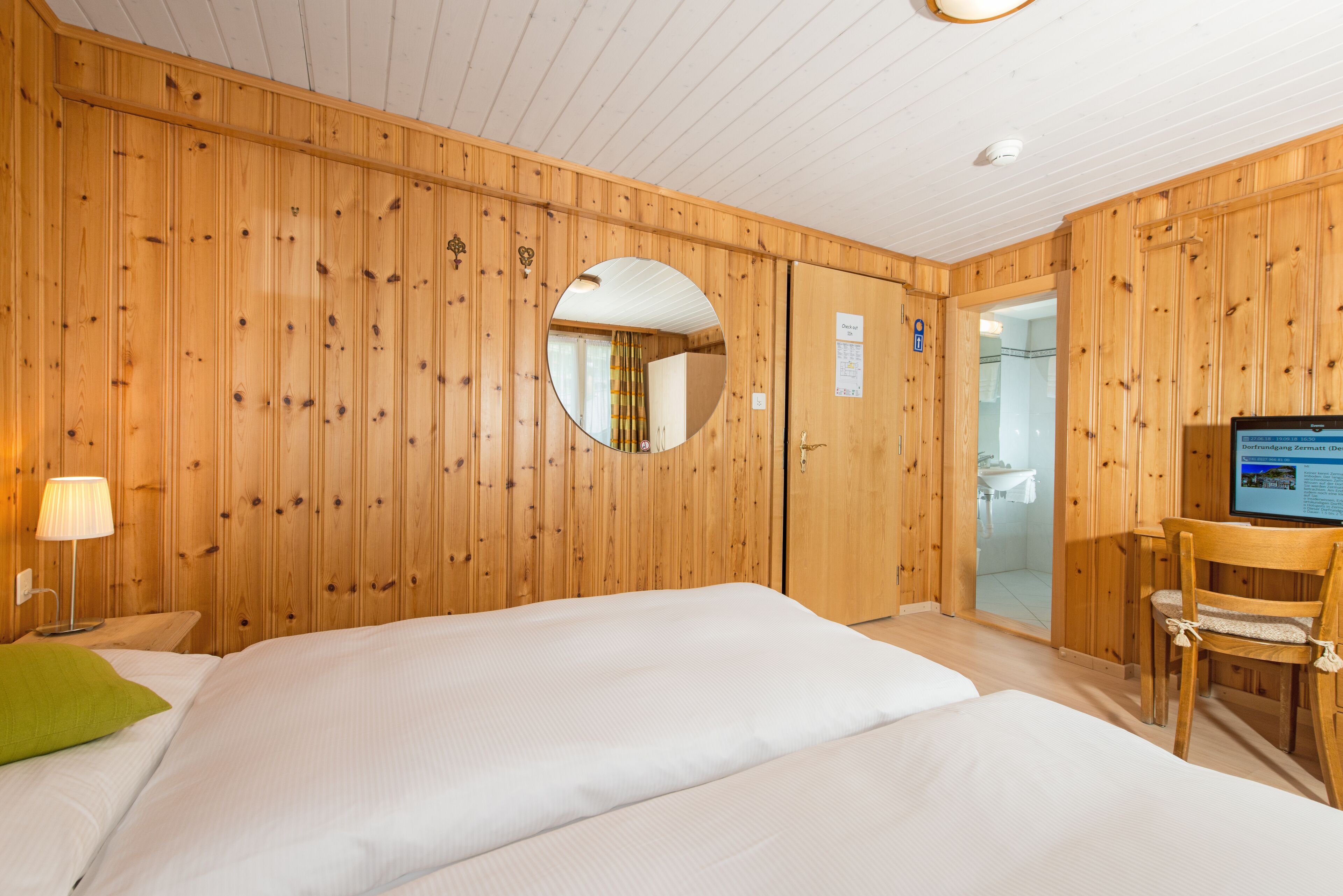 A wooden-paneled room with a bed, a mirror, a chair, and a television.