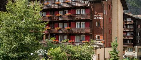 Un hotel de varios pisos con balcones decorados con flores, con montañas al fondo.