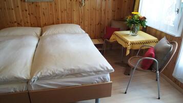 Ein Zimmer mit Holzwänden, einem Bett, einem kleinen Tisch mit Blumenvase und einem Sessel.