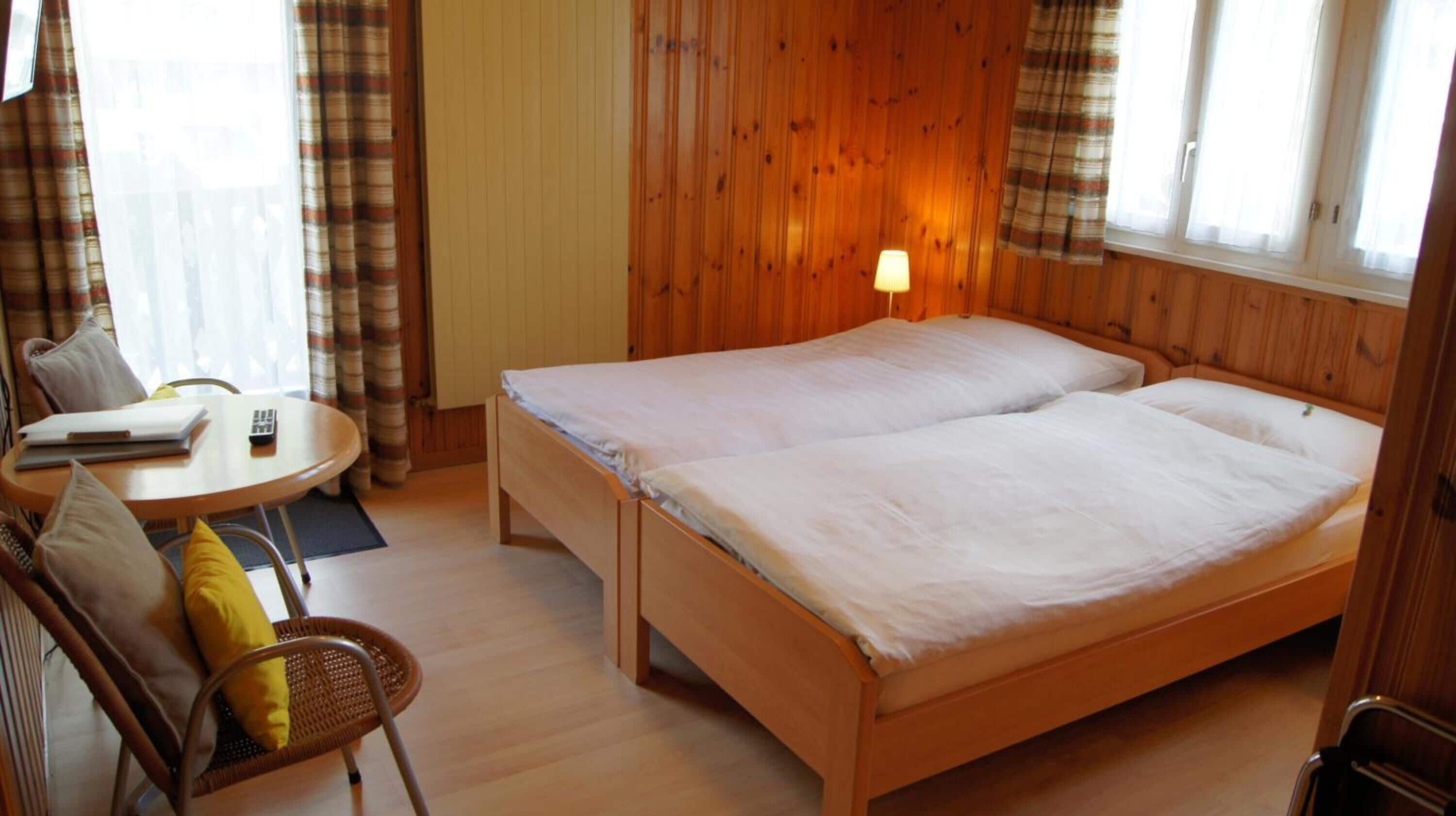 Uma cama de casal com cabeceira de madeira, uma mesinha de cabeceira e uma cadeira com almofada.