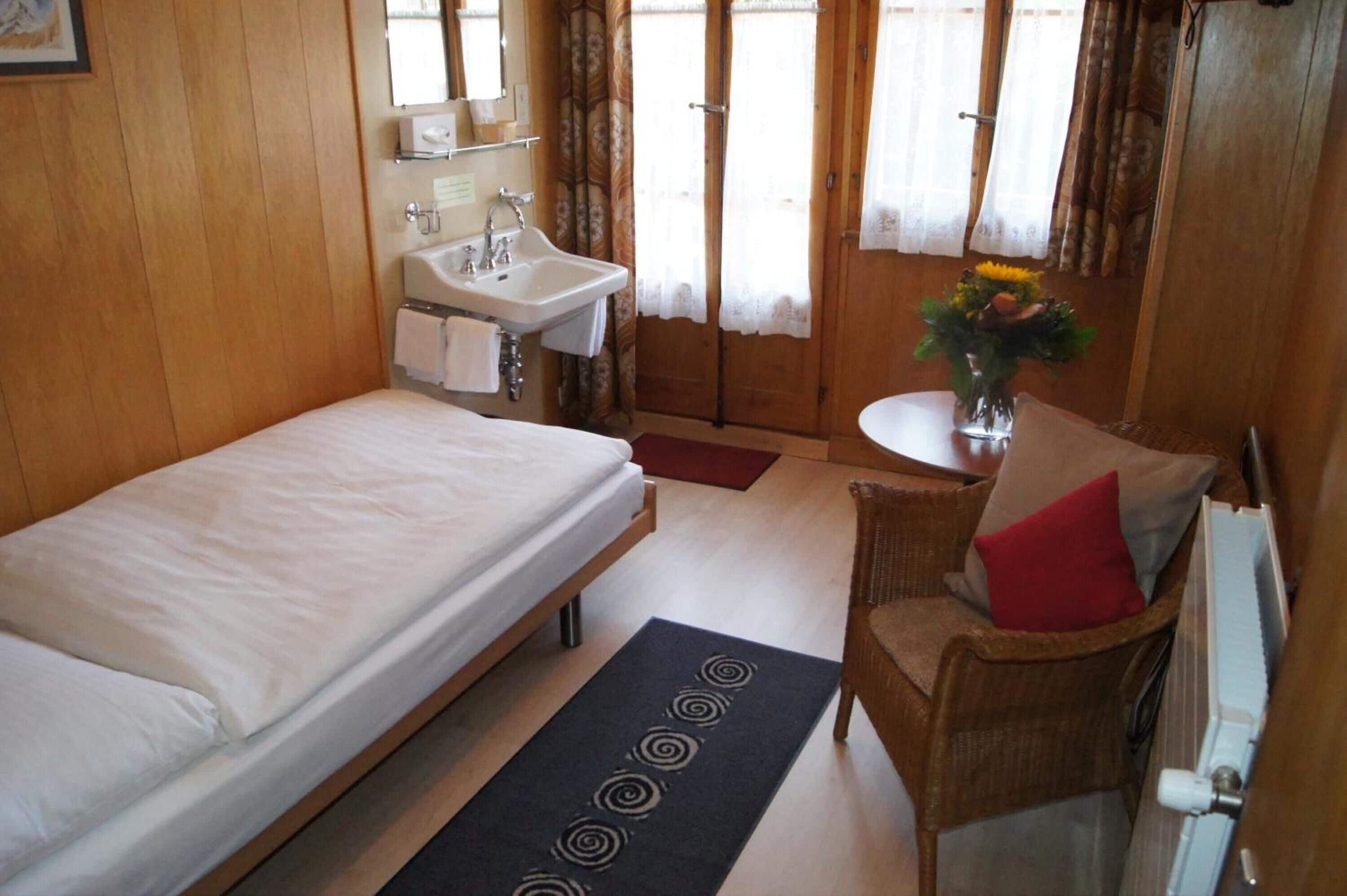 A bedroom with a bed, a sink, a chair, and a small table with a vase of flowers.
