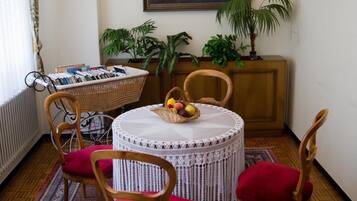 Un coin repas avec une table ronde, quatre chaises, un lustre, un tableau et des plantes en pot.