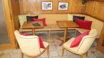A cozy seating area with a wooden bench and two chairs, a small table, and a tiled floor.