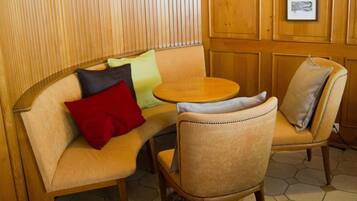 Una zona de estar acogedora con un banco de madera y una mesa redonda, con un tapete estampado y cuadros enmarcados en la pared.