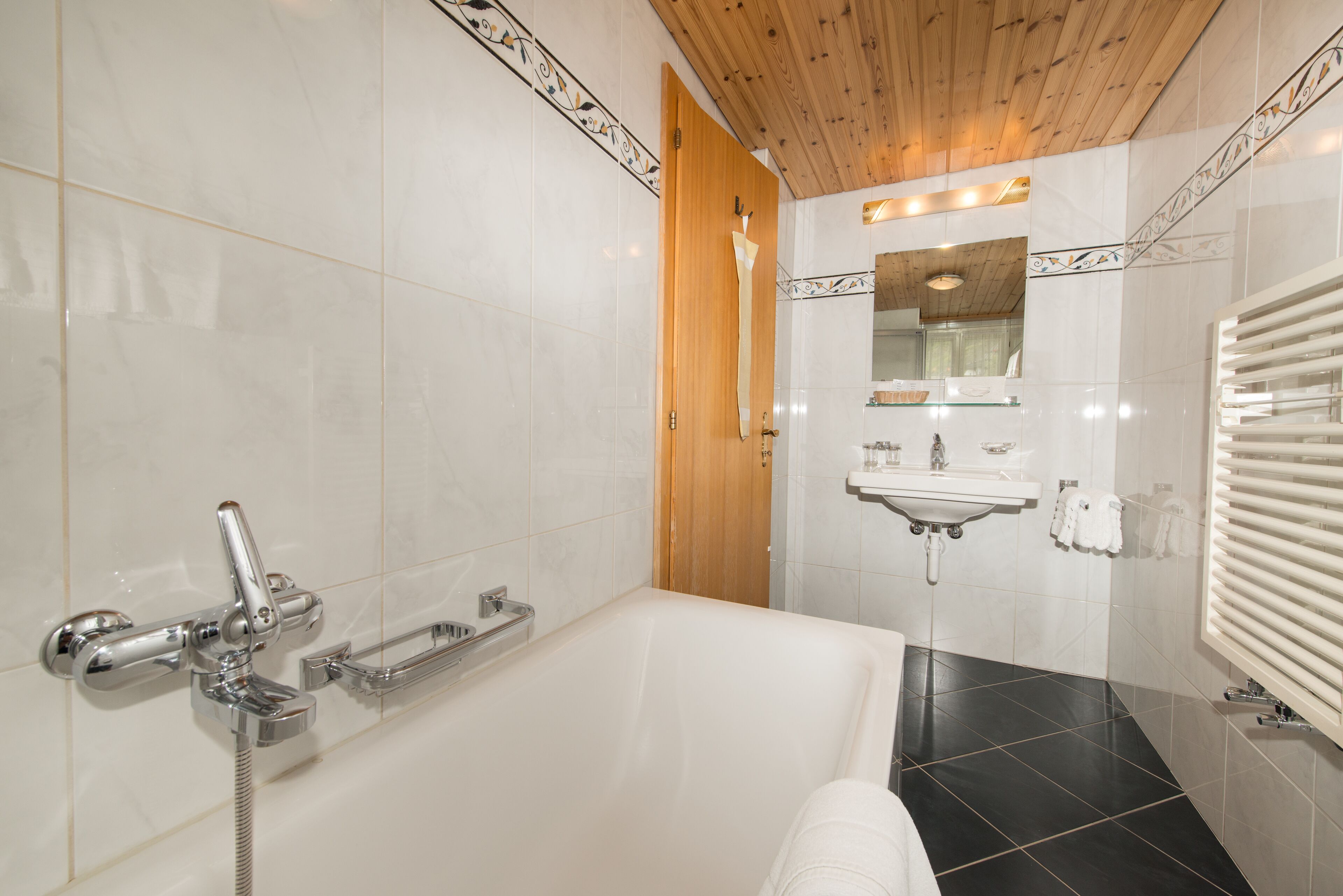 Un baño moderno con una bañera grande, techo de madera y suelo de baldosas.