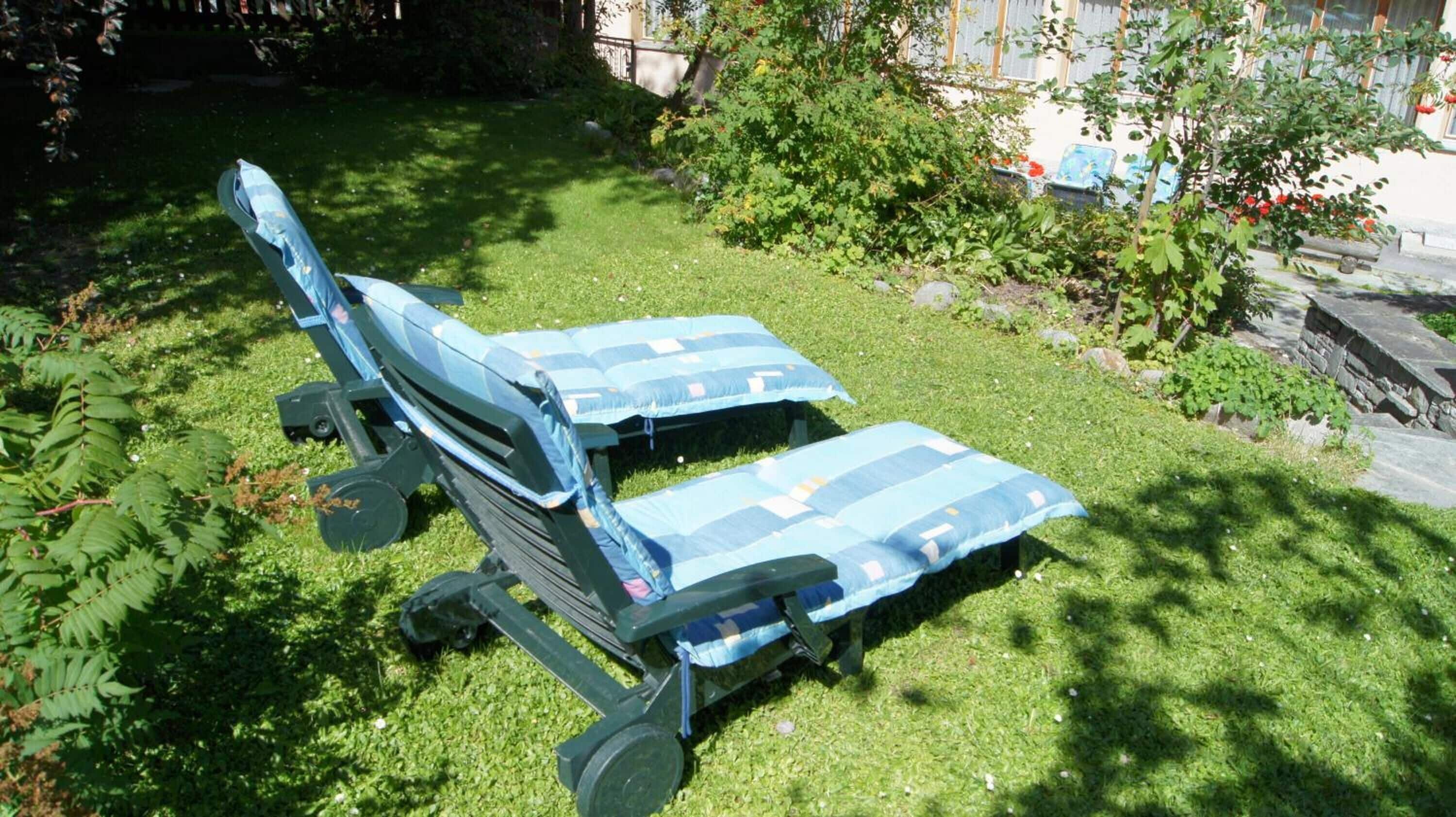 Two outdoor lounge chairs with blue cushions in a grassy garden area.