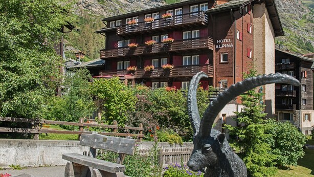 Un hotel con varios balcones, una banca de madera y una estatua.