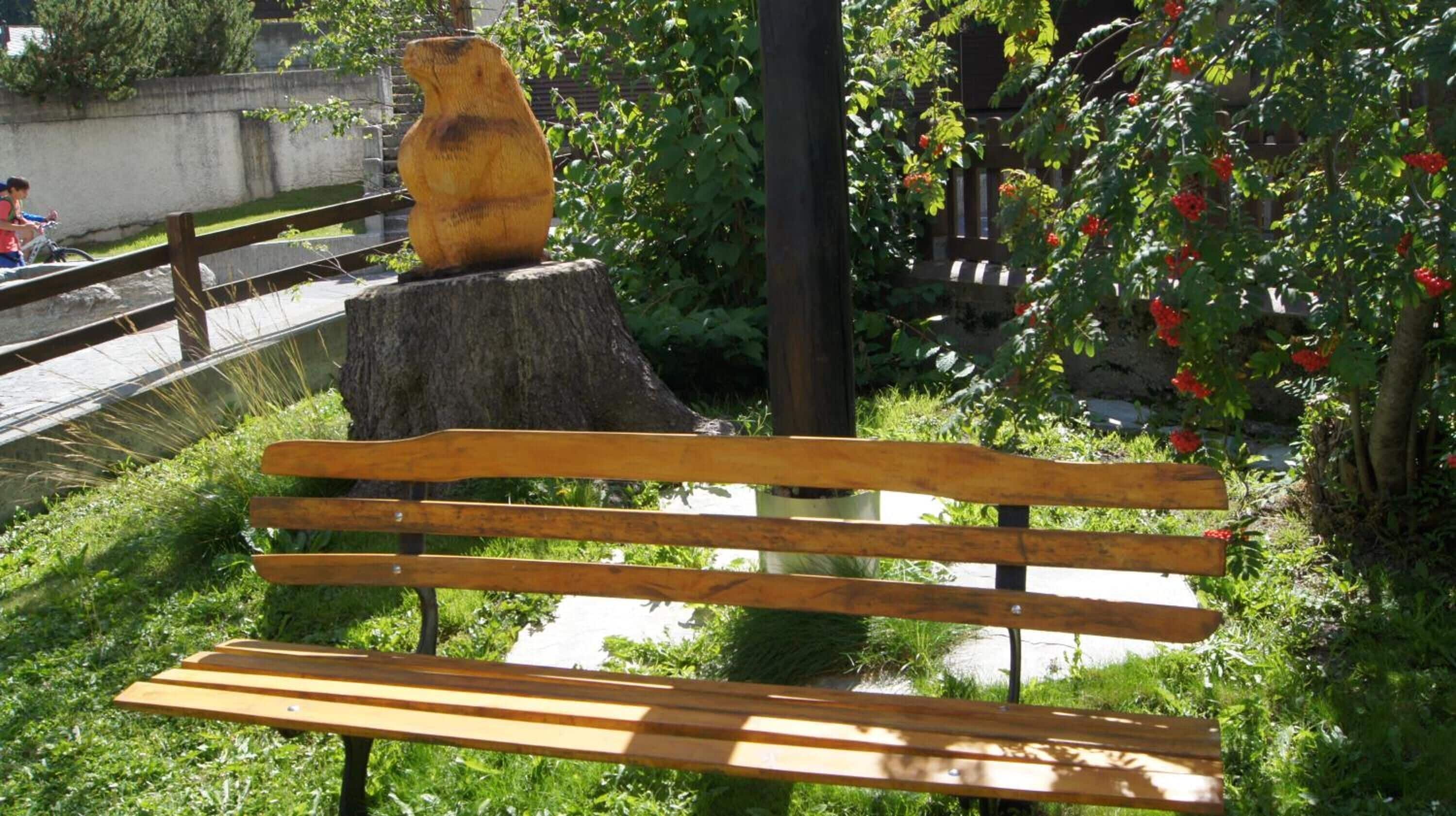Un banco de madera con una escultura de oso tallado en un tocón de árbol en un parque.
