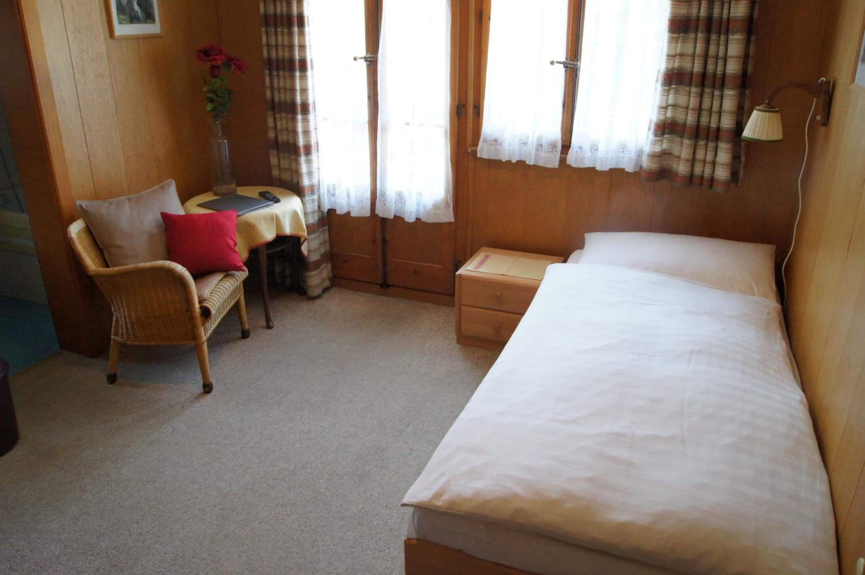 Una habitación pequeña y acogedora con una cama individual, una silla, una mesita y una lámpara.