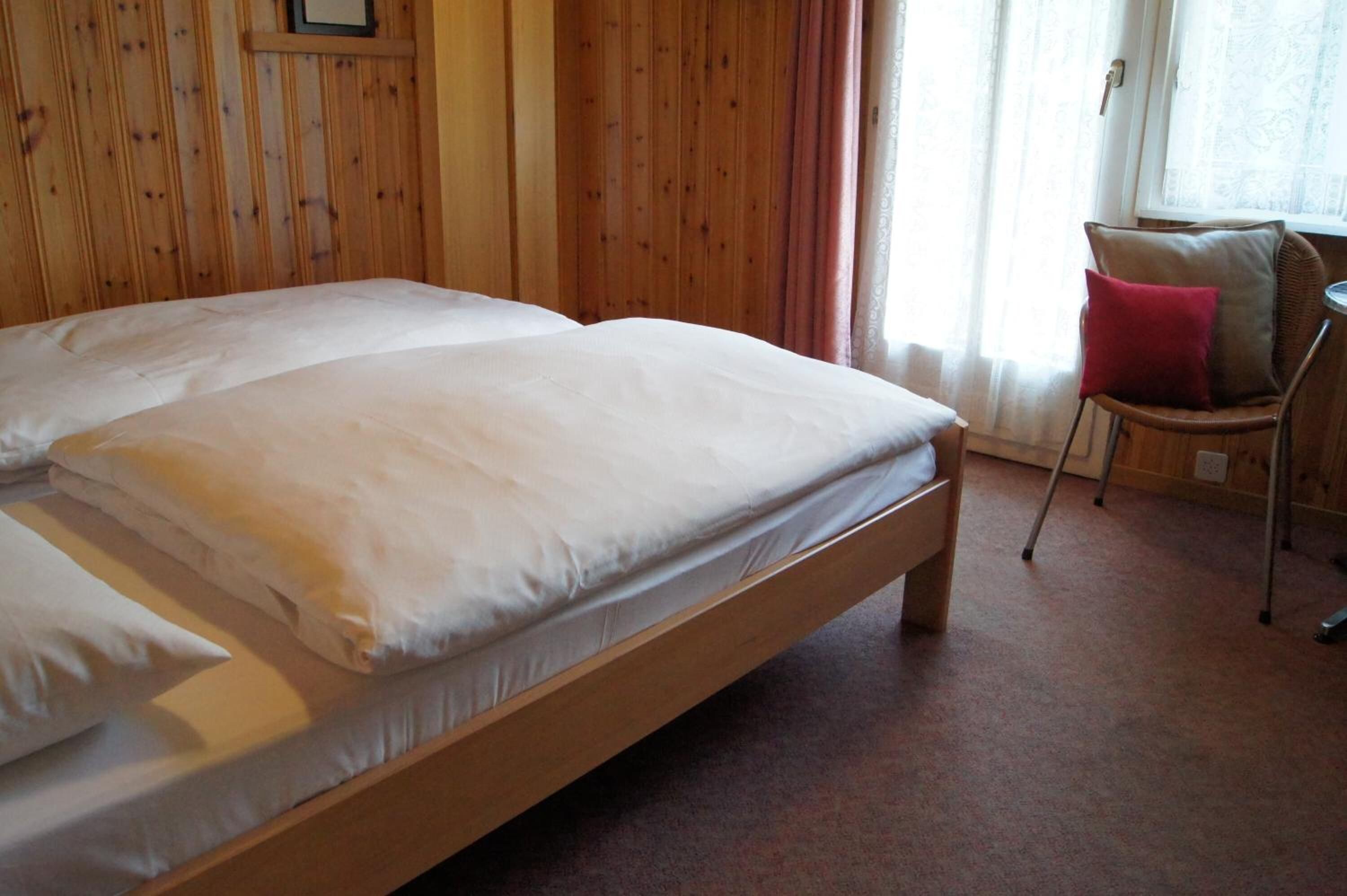 A wooden bed with white linens in a room with wooden walls and a window with curtains.