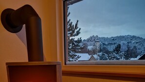 A wood-burning stove with a visible fire, a window with a view of a snowy landscape, and a basket with items on the floor.