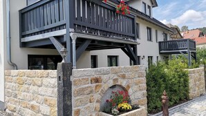 A two-story building with a balcony, stone wall, and flower bed.