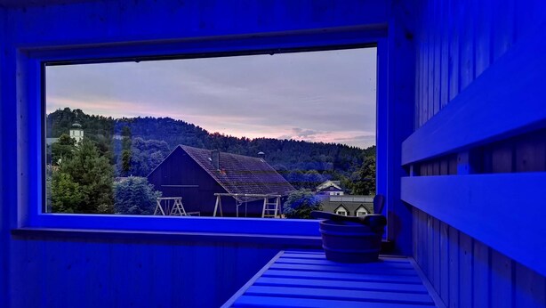 A room with a large window overlooking a rural landscape, a wooden bench, and a small table.