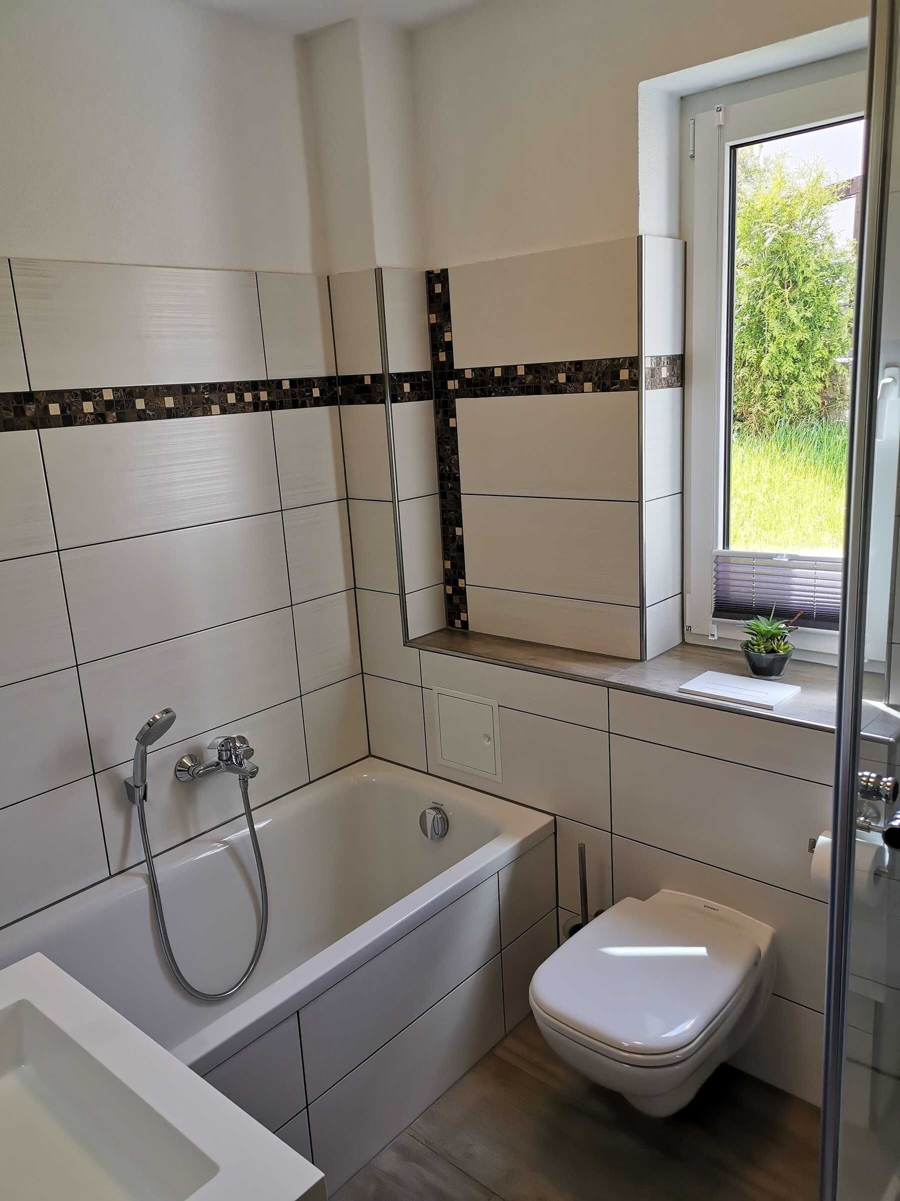 Et moderne badeværelse med badekar, toilet og et vindue med udsigt til grønne omgivelser.