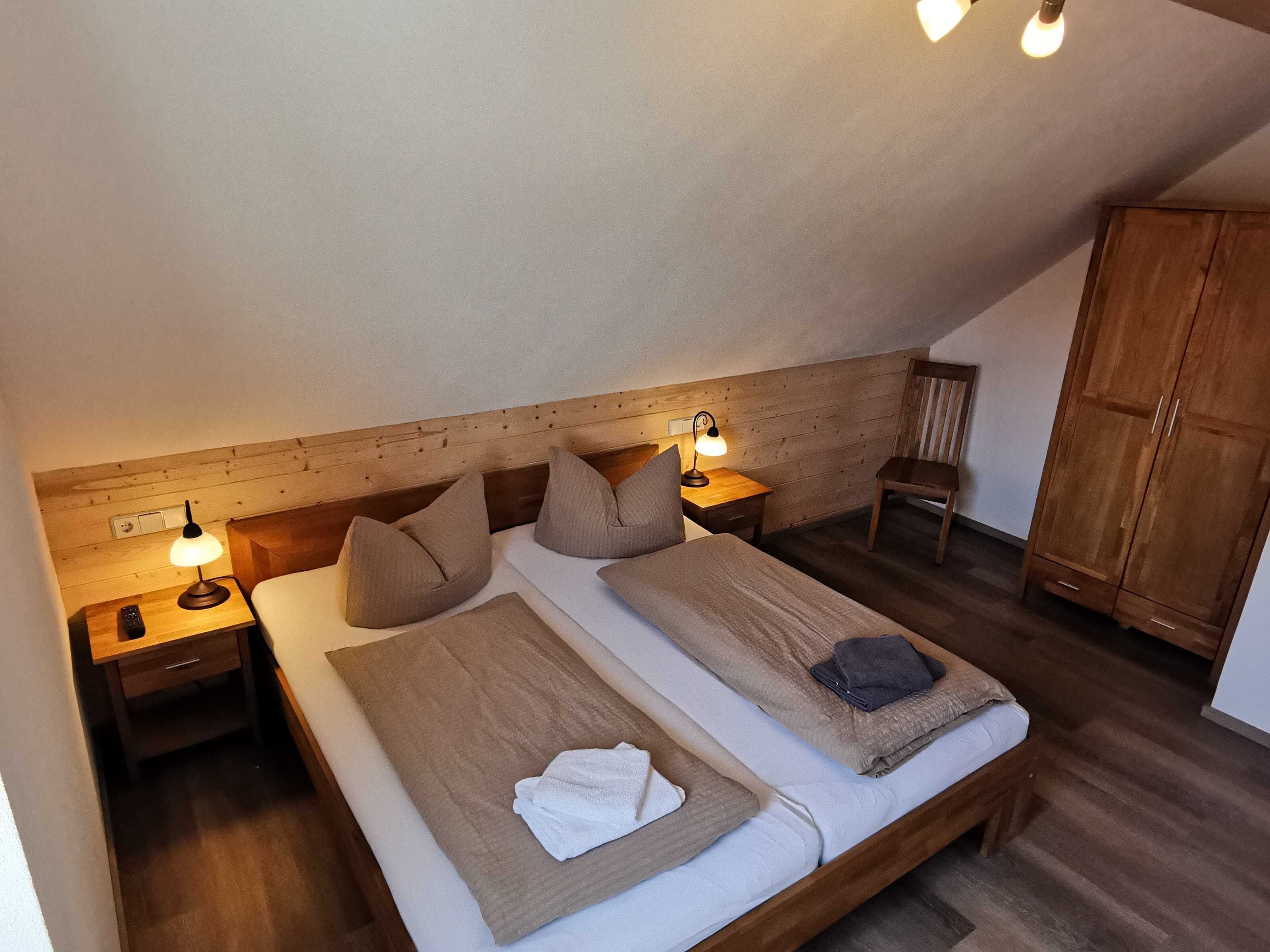 Ein Schlafzimmer mit zwei Betten, einem Holzkopfstück, Nachttischlampen, einem hölzernen Kleiderschrank und einem kleinen Tisch mit Lampe.