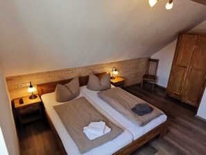 Un dormitorio con dos camas, cabeceros de madera, lámparas de noche, un armario de madera y una mesita con lámpara.