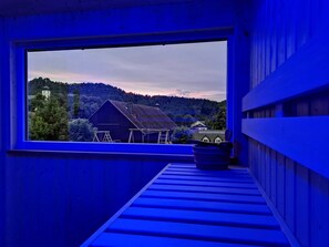 A room with a large window overlooking a rural landscape, a wooden bench, and a small table.