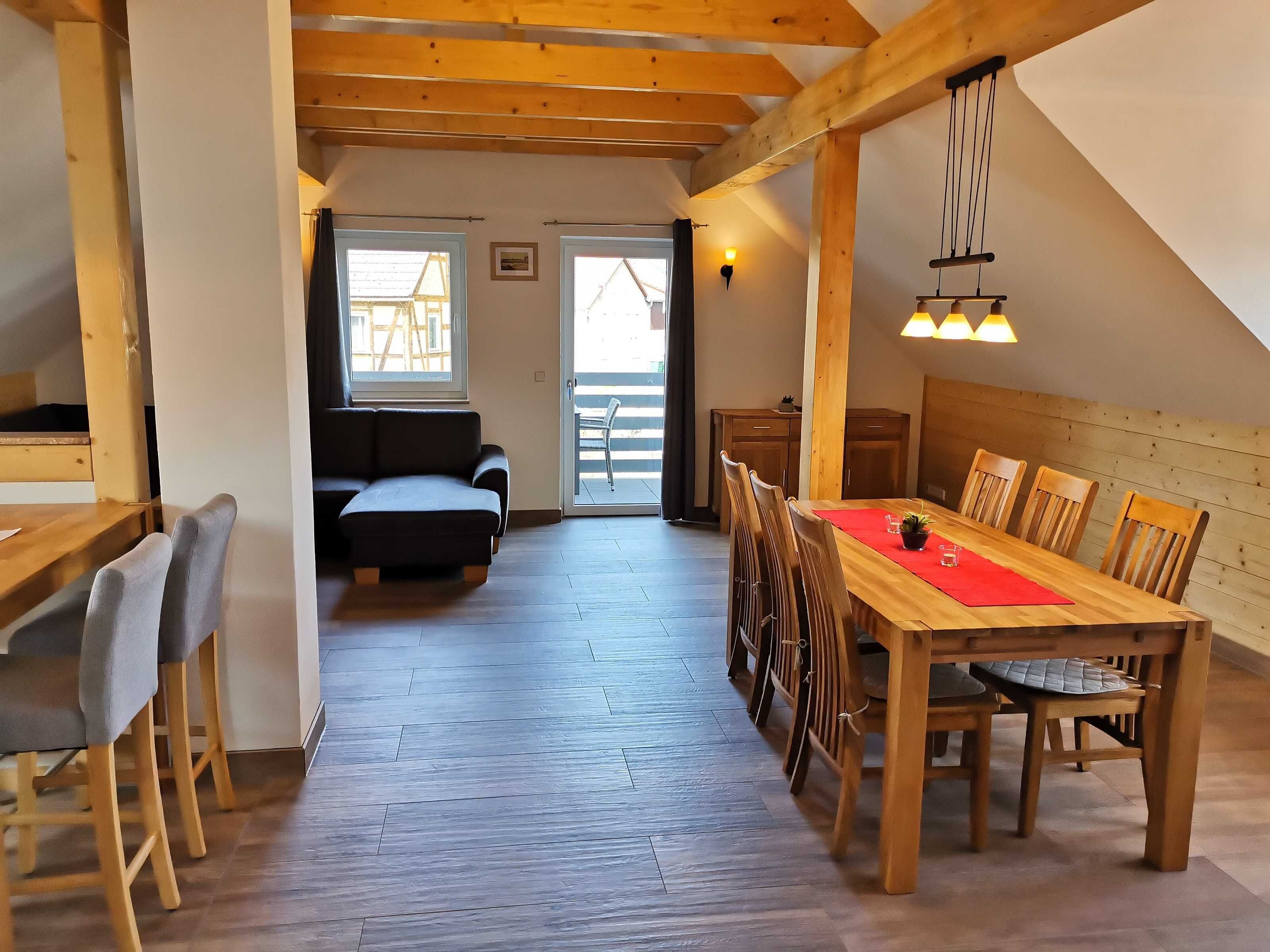 Accogliente camera mansardata con zona pranzo, travi in legno e vista attraverso un'ampia finestra.