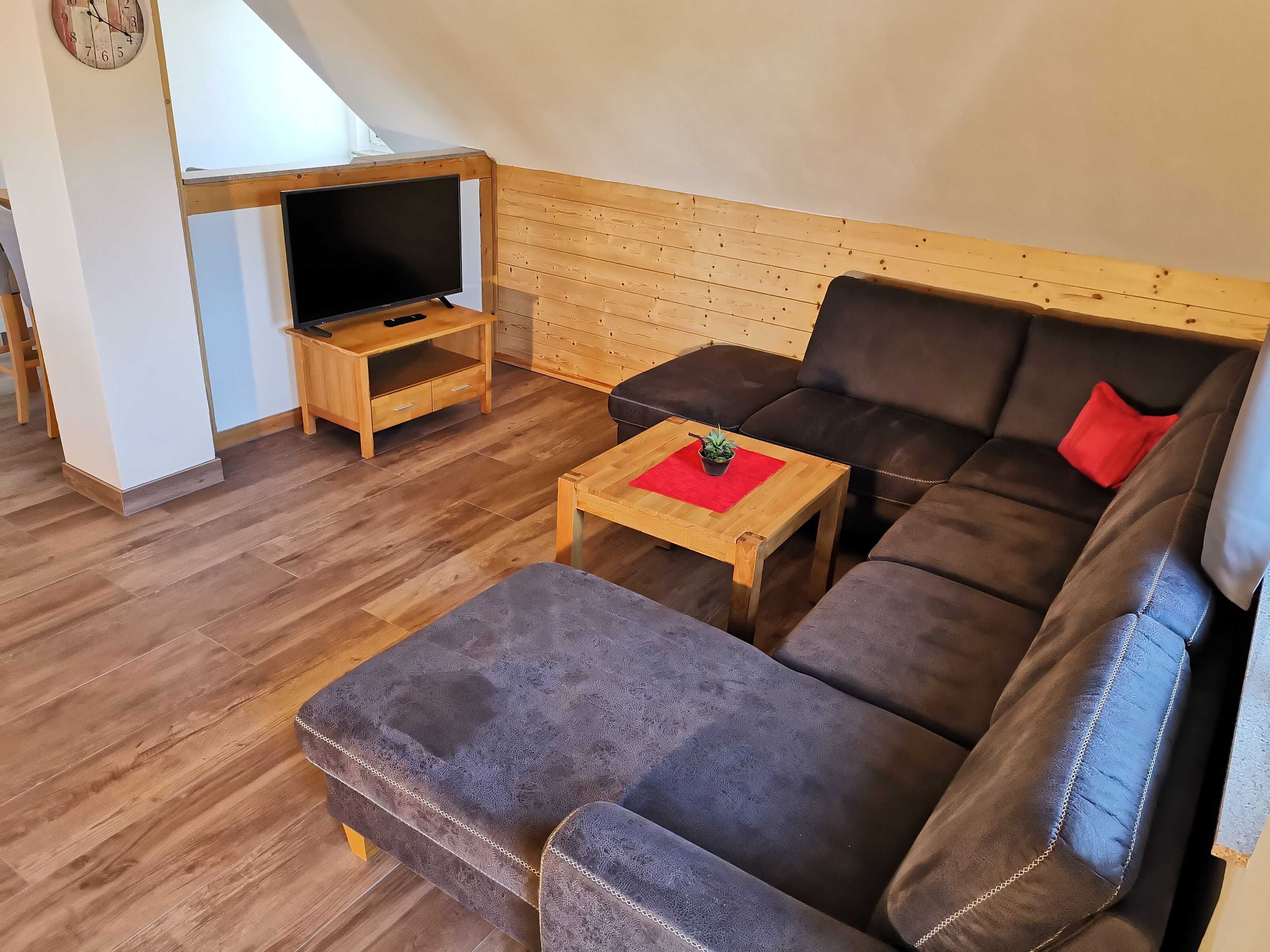 Una sala de estar acogedora con piso de madera, un sofá marrón, una mesita de madera y un televisor sobre un mueble.
