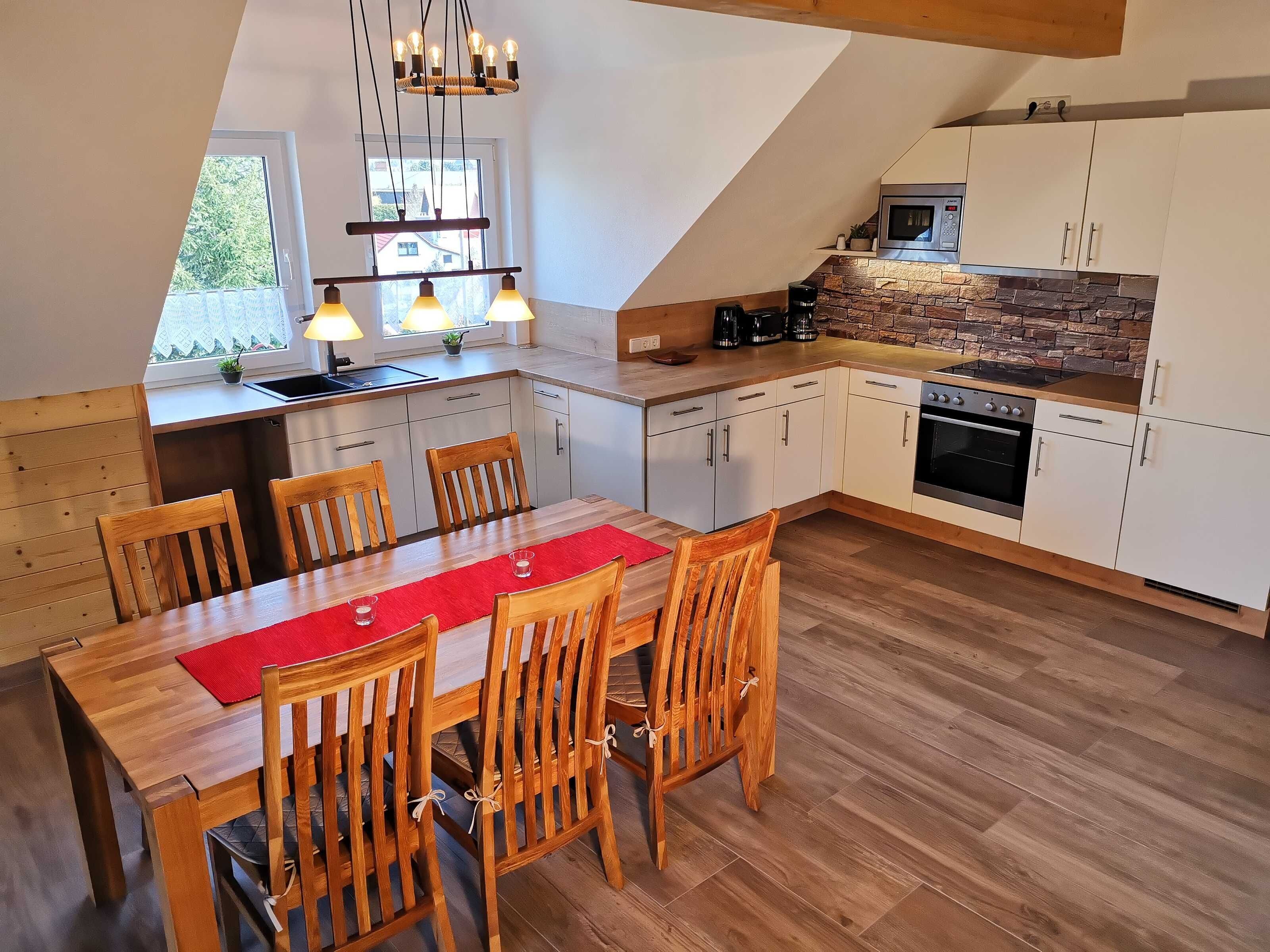 Una cocina moderna con armarios blancos, una mesa de comedor de madera y un mantel individual rojo.
