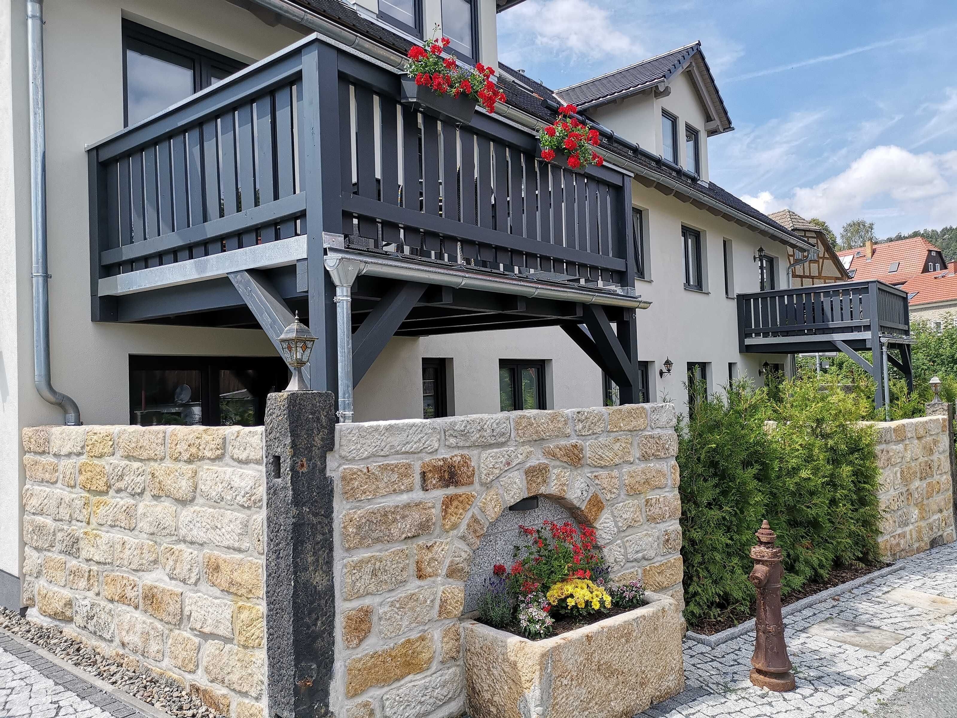 Ein zweistöckiges Gebäude mit Balkon, Steinmauer und Blumenbeet.
