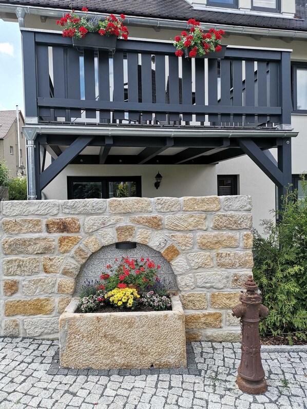 Un edificio con fachada de piedra, un balcón con macetas de flores y un hidrante.