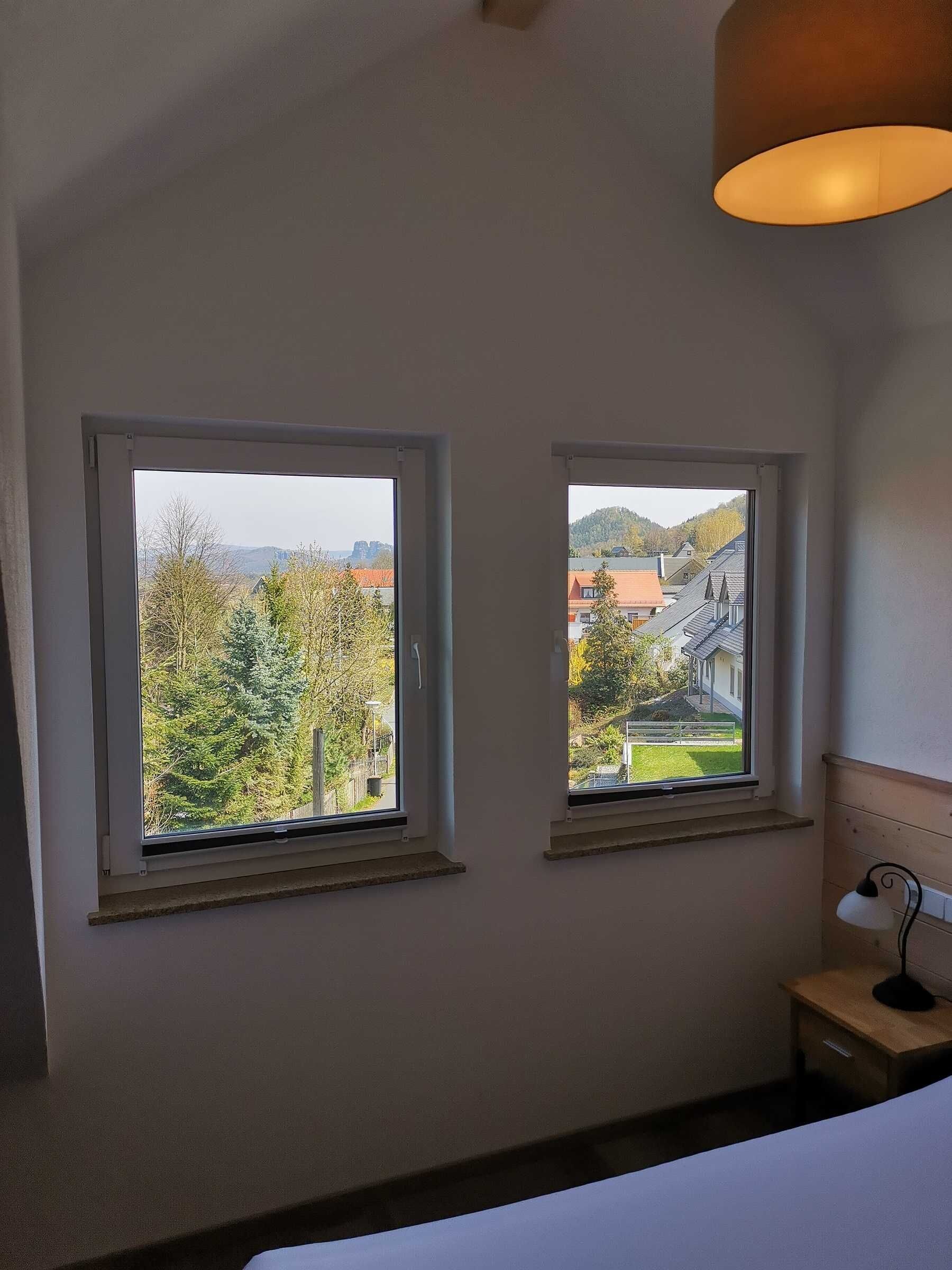 Un dormitorio con dos ventanas, una lámpara de noche y vistas a una zona residencial.