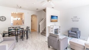 A modern living room with a dining area, a fireplace, and a staircase.