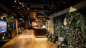A modern reception area with a wooden floor, seating, a reception desk, and a wall adorned with plants. - Apartment Flamengo mit Küchenzeile - Rioca Vienna Posto 1 (Wien)