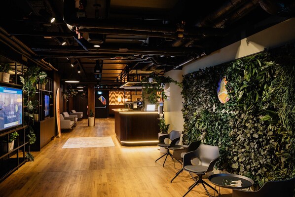 A modern reception area with a wooden floor, seating, a reception desk, and a wall adorned with plants.