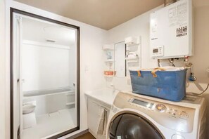 A laundry room with a washing machine, a dryer, a blue laundry basket, and a water heater. - Stardust (Sapporo)