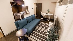 Un espace de vie compact comprenant un coin cuisine, un canapé, une petite table ronde et une plante en pot.