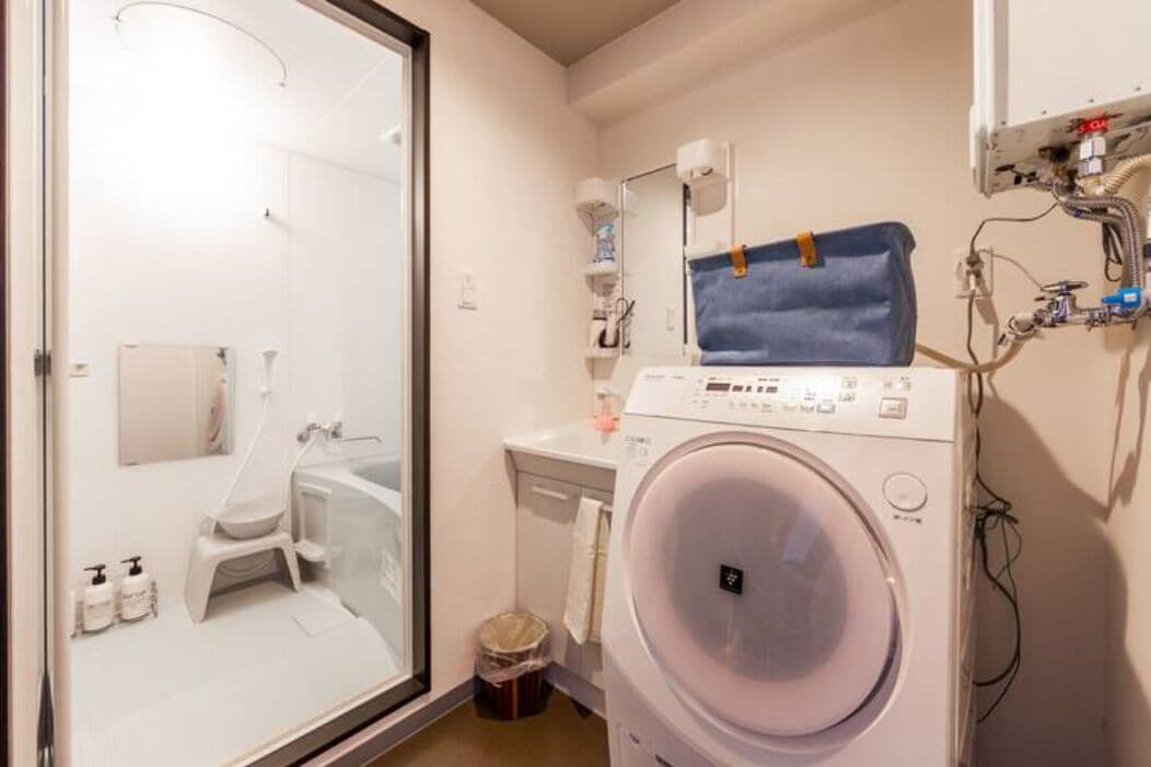 Une salle de bain compacte avec une douche à parois de verre, un lave-linge et un petit lavabo.