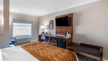 Een hotelkamer met een bed, een bureau met een computer, een televisie en een raam met zonwering.