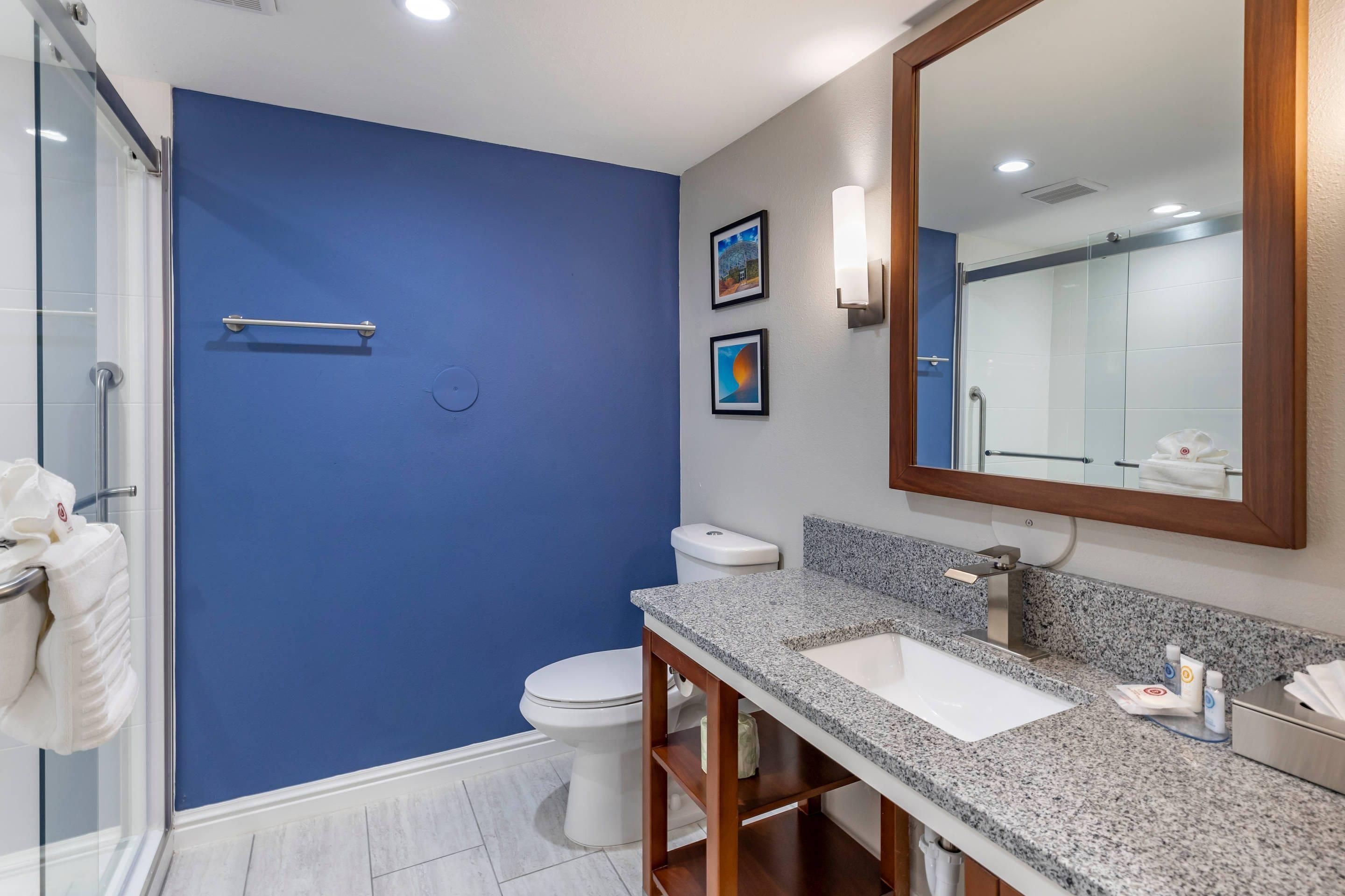 A bathroom with a blue accent wall, a white toilet, a sink with a granite countertop, and a mirror.