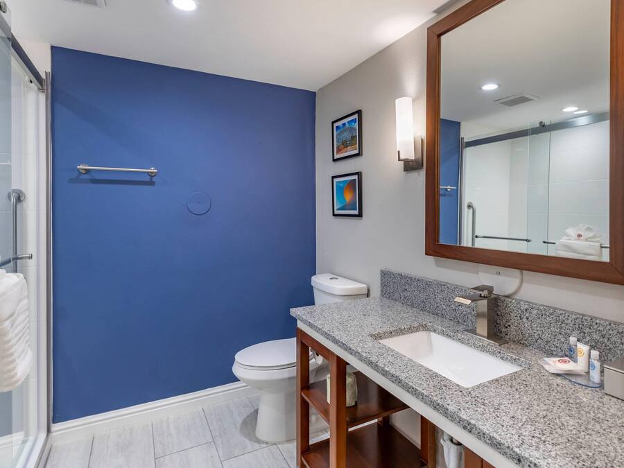 Un baño con una pared de acento azul, un inodoro blanco, un lavabo con encimera de granito y un espejo.
