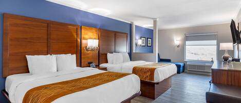 A hotel room with two beds, a desk, and a window.