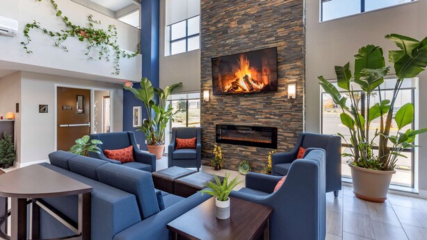A modern lobby with a stone fireplace, blue sofas, and potted plants. - Comfort Suites St. Louis - Sunset Hills (St. Louis)