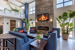 A modern lobby with a stone fireplace, blue sofas, and potted plants. - Comfort Suites St. Louis - Sunset Hills (St. Louis)