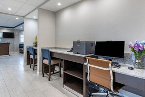 Un espace d’accueil d’hôtel comprenant un comptoir, un ordinateur, une imprimante, des chaises et un vase avec des fleurs.
