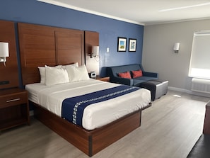 Une chambre d’hôtel avec un grand lit, un canapé, une petite table et une fenêtre avec des stores.