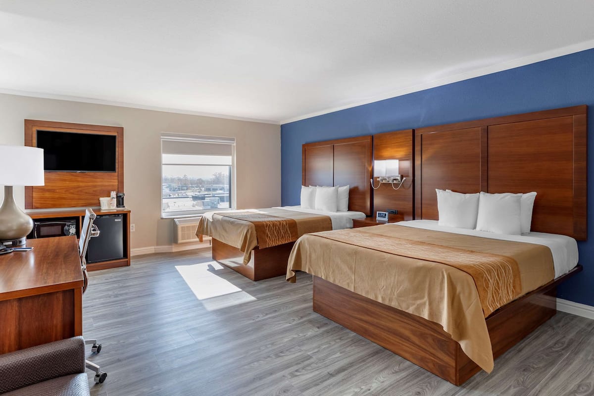 A hotel room with two beds, a desk with a lamp, a TV, and a view of the city.