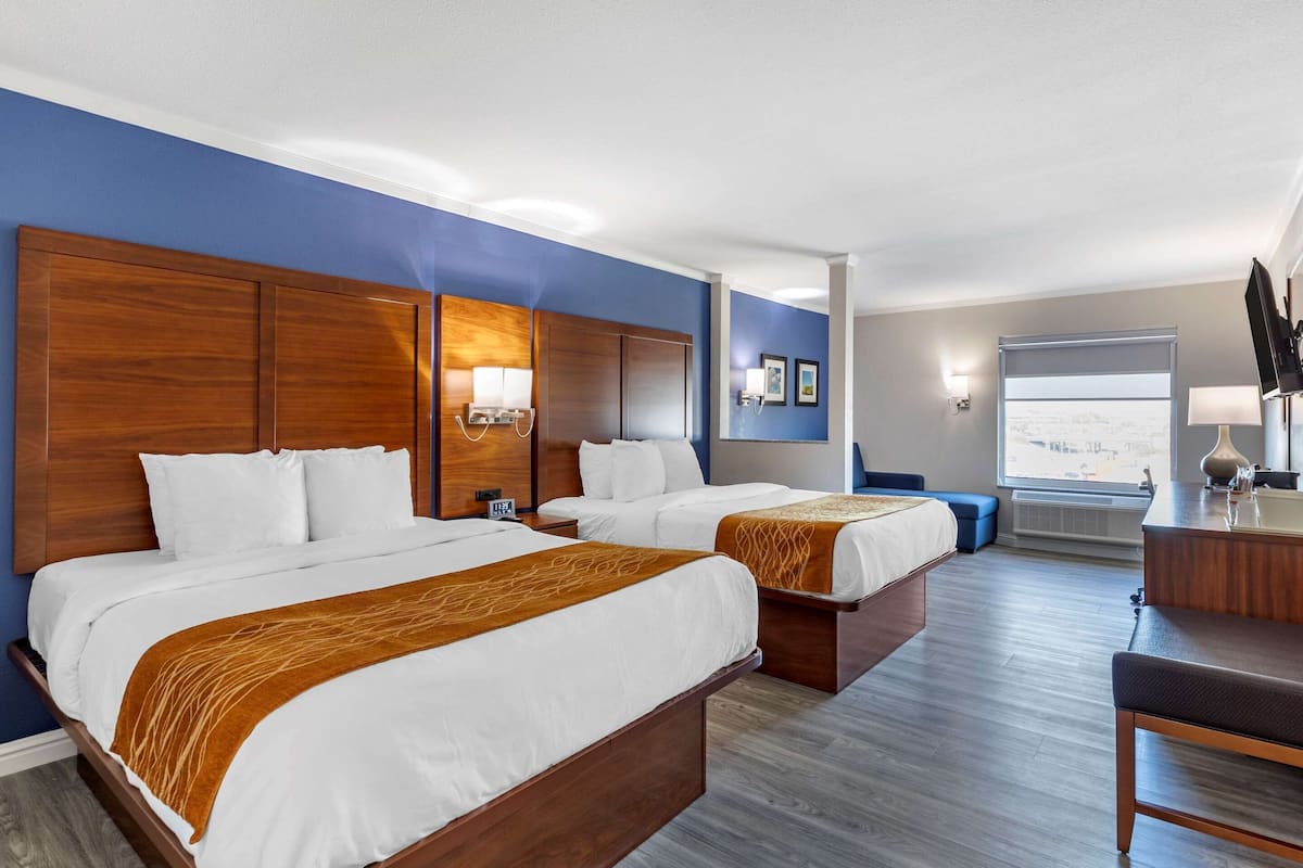 A hotel room with two beds, a desk, a chair, and a large window.