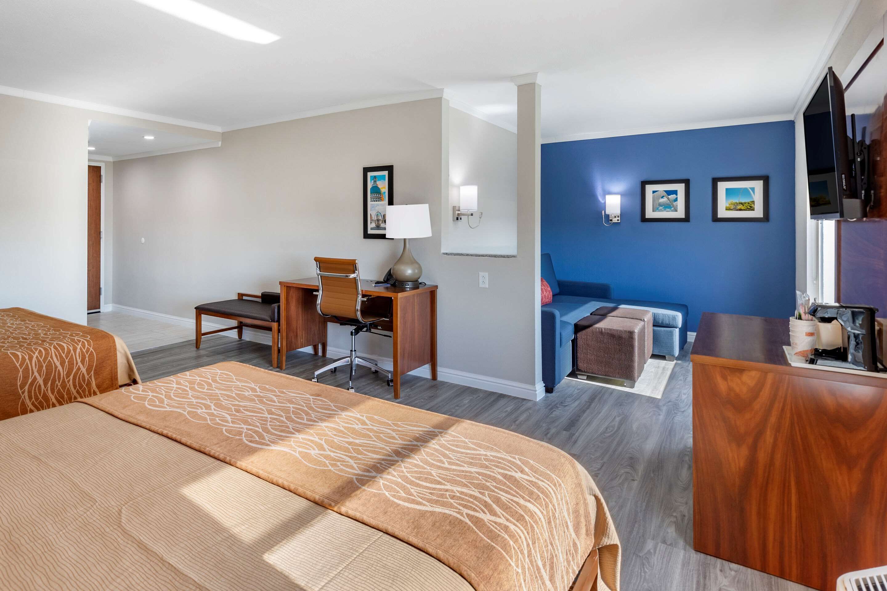 A hotel room with two beds, a desk, a chair, a sofa, and a TV.
