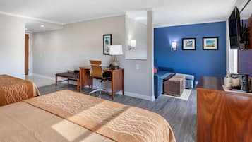 A hotel room with two beds, a desk, a chair, a sofa, and a TV.