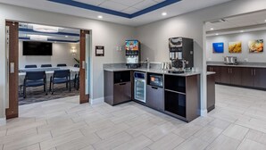A modern kitchen with a coffee machine, microwave, and refrigerator. There is a dining area with tables and chairs. - Comfort Suites St. Louis - Sunset Hills (St. Louis)